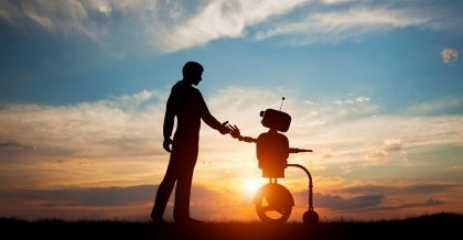 Ein Mensch gibt einem Roboter vor einem Sonnenuntergang die Hand.