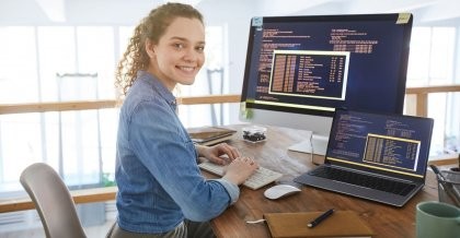 Eine PHP Programmiererin sitzt an ihrem Schreibtisch vor zwei Rechnern und programmiert.