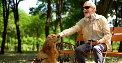 Blinder Mann auf Parkbank streichelt Hund und nutzt mobil barrierefreie Webseite
