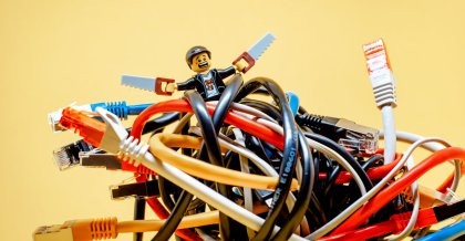 Ein Lego Männchen steht mit zwei Sägen in einem Gewirr aus Netzwerkkabeln. Der kleine IT-Profi ist bereit zur IT-Wartung.