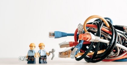 Zwei Legomännchen in Bauarbeiter-Montur. Sie haben kleine Werkzeuge in den Händen und stehen einem riesigen Wust aus Kabel gegenüber. Sie bereiten sich auf eine IT-Dienstleistung vor.