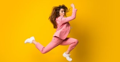 Eine junge Frau in legerem rosa Anzug. Sie sprintet dynamisch vor gelbem Hintergrund. Sie betreibt Performance-Optimierung.