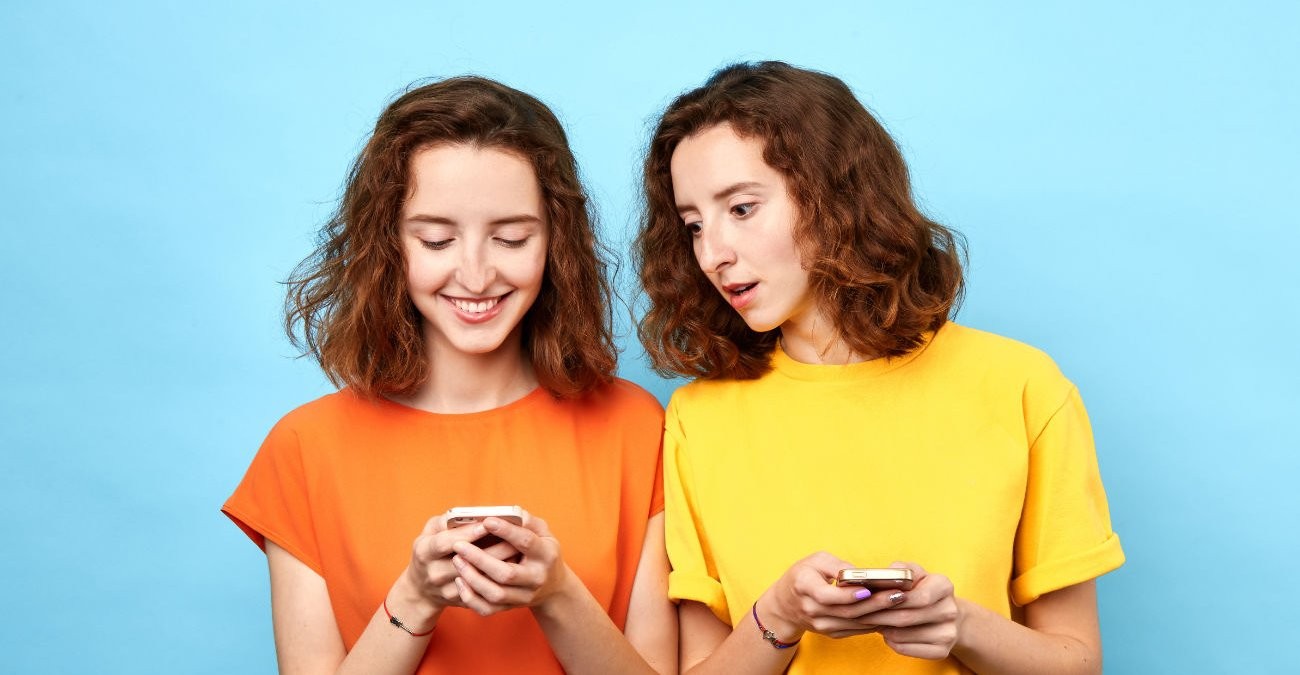 Zwei junge Frauen, Zwillinge, sehen auf ihre Handys. Ein Symbolbild für die Google KI Gemini.