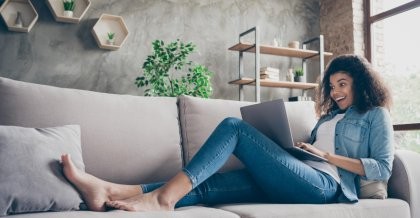 Eine junge Frau sitzt mit ausgestreckten Beinen auf der Couch. Auf ihrem Schoß ein Laptop. Sie schreibt begeister User generated Content.